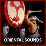 traditional asian drummer standing and holding two drum sticks up above his head about to hit a very large vertical traditional white drums with red marking on and around it